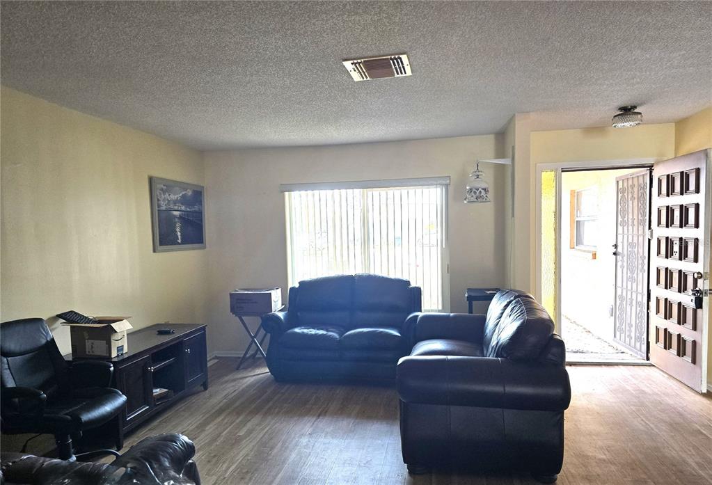 A living room features dark leather furniture, wood-look flooring, and an open front door — 10641 TIMBER LANE, PORT RICHEY, FL