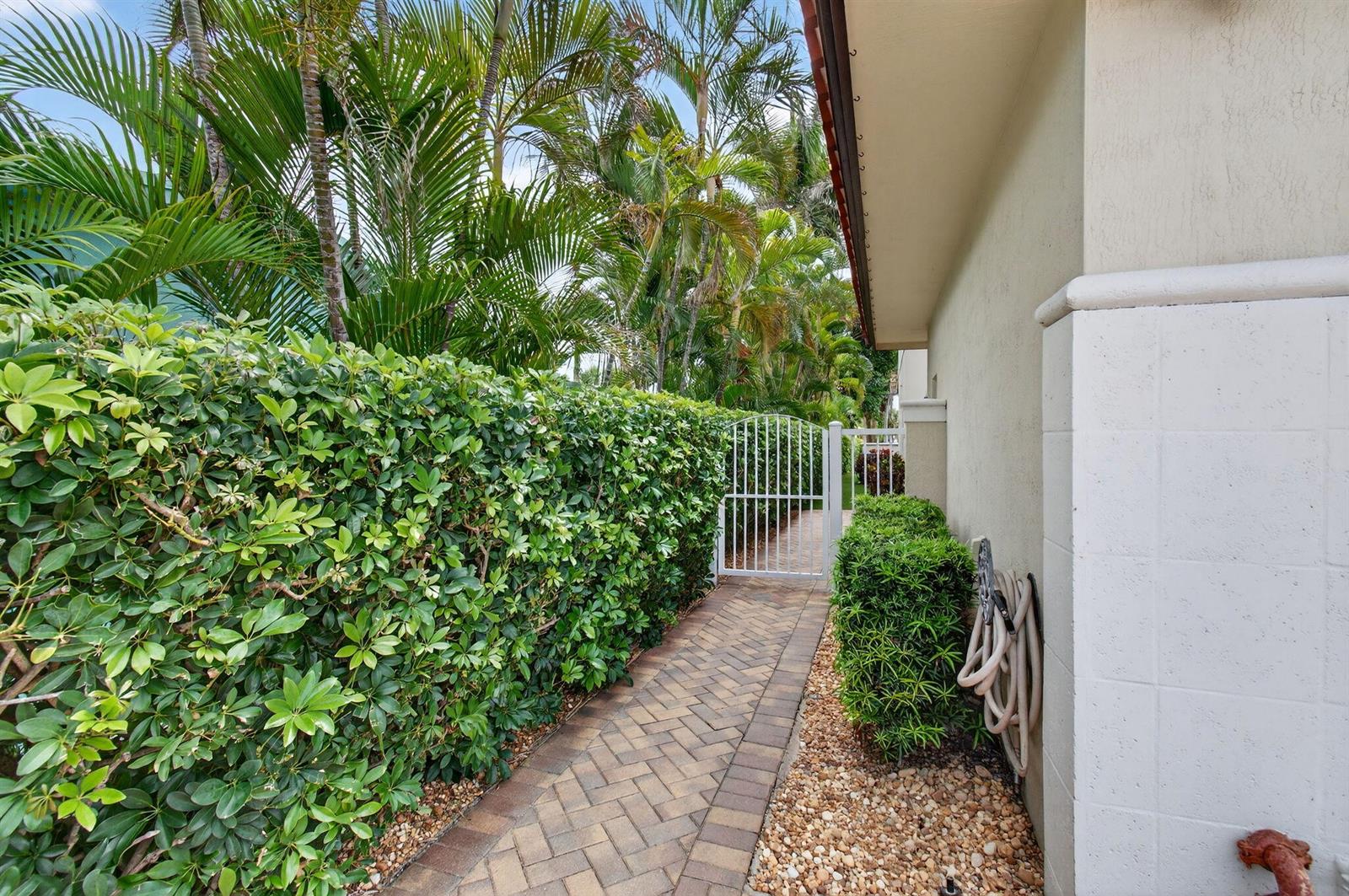 A paved walkway leads past a hedge and a white gate along the side exterior — 1942 NE 6th Street # C, Deerfield Beach FL 33441, DEERFIELD BEACH, FL