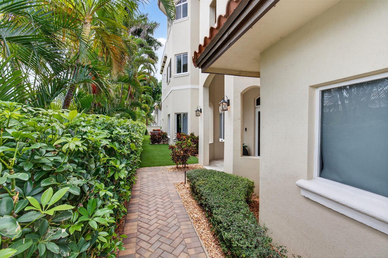 A paved walkway runs alongside a stucco building exterior with landscaping and palm trees — 1942 NE 6th Street # C, Deerfield Beach FL 33441, DEERFIELD BEACH, FL