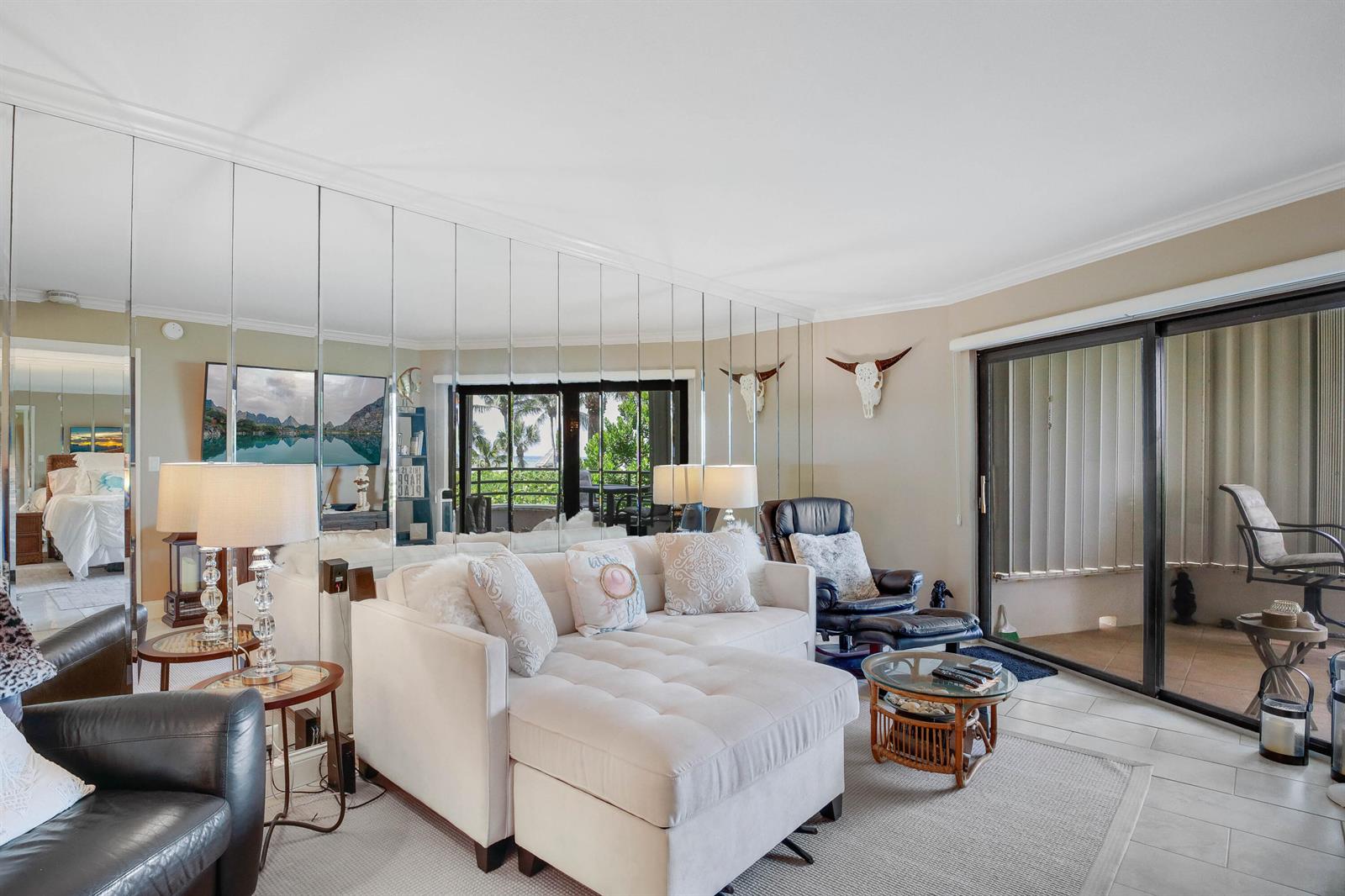 A living room features a mirrored wall, a white sectional sofa, and sliding glass doors — 420 Celestial Way # 204, Juno Beach FL 33408, JUNO BEACH, FL