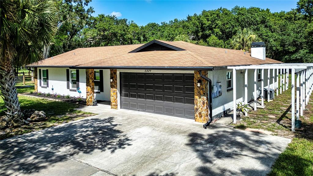 A single-story house with a white stucco exterior, stone accents, and a brown shingled roof — 3309 YELLOWKNIFE CIRCLE, WIMAUMA, FL