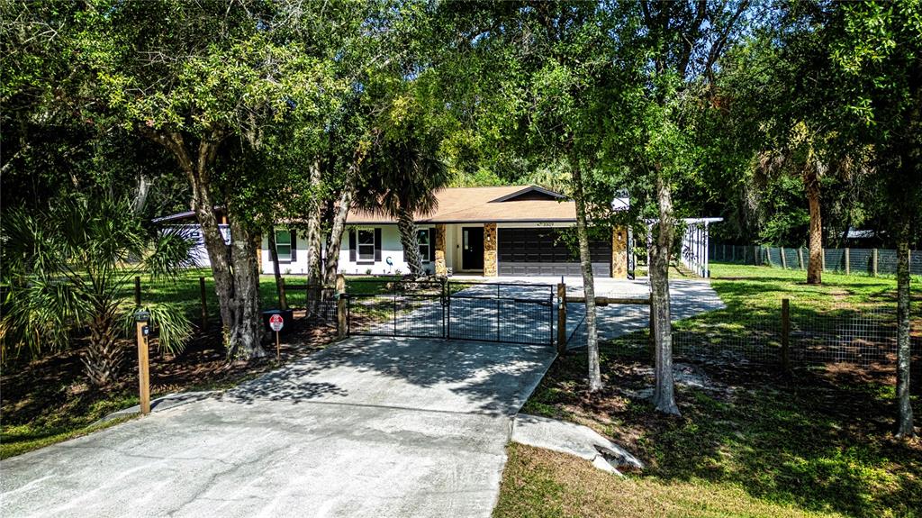 A single-story house with a gated concrete driveway, a two-car garage, and surrounding trees — 3309 YELLOWKNIFE CIRCLE, WIMAUMA, FL