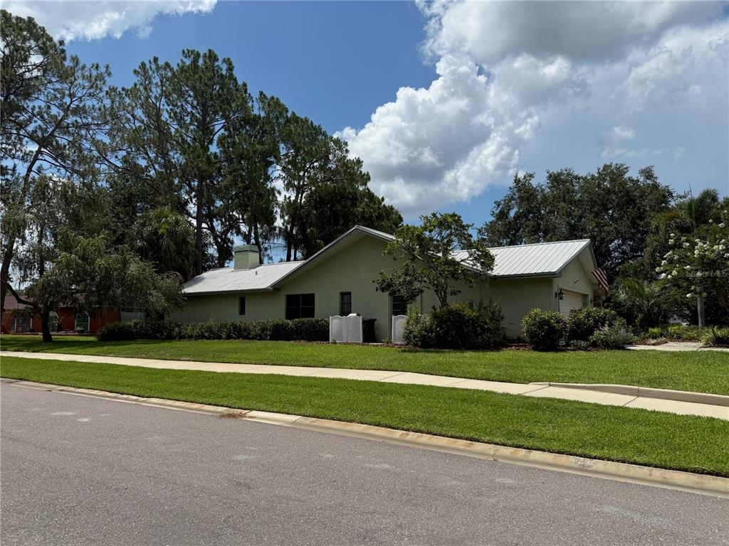 A single-story house with a light green exterior and a metal roof sits on a lawn — 2215 TONIWOOD LANE, PALM HARBOR, FL