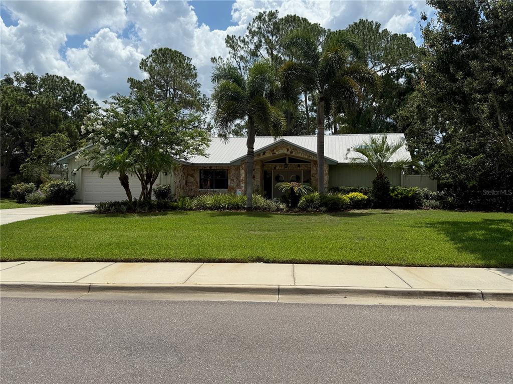 A single-story house with a metal roof, stone facade, and palm trees in the front yard — 2215 TONIWOOD LANE, PALM HARBOR, FL