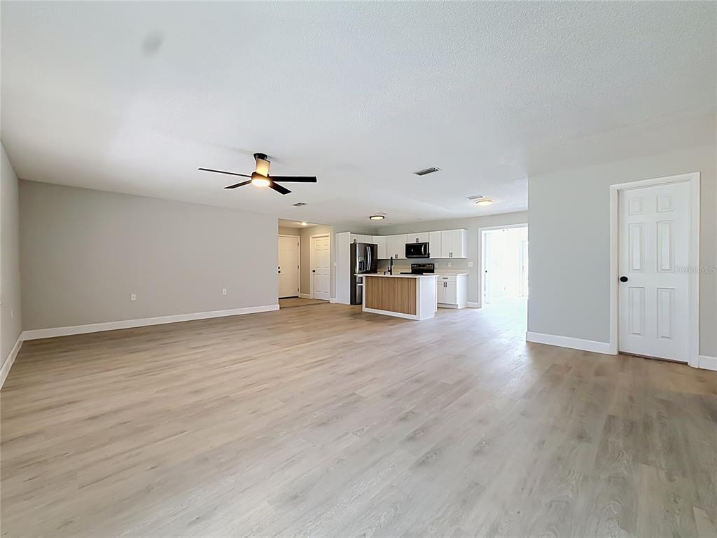 An open-concept living area features light wood-look flooring, a ceiling fan, and a modern kitchen — 501 ROSE AVENUE, FRUITLAND PARK, FL