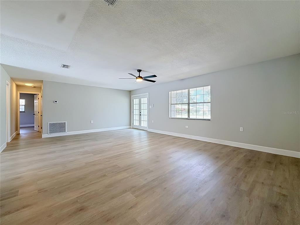 A spacious, empty living room features light-colored wood-look flooring, gray walls, and a ceiling fan — 501 ROSE AVENUE, FRUITLAND PARK, FL