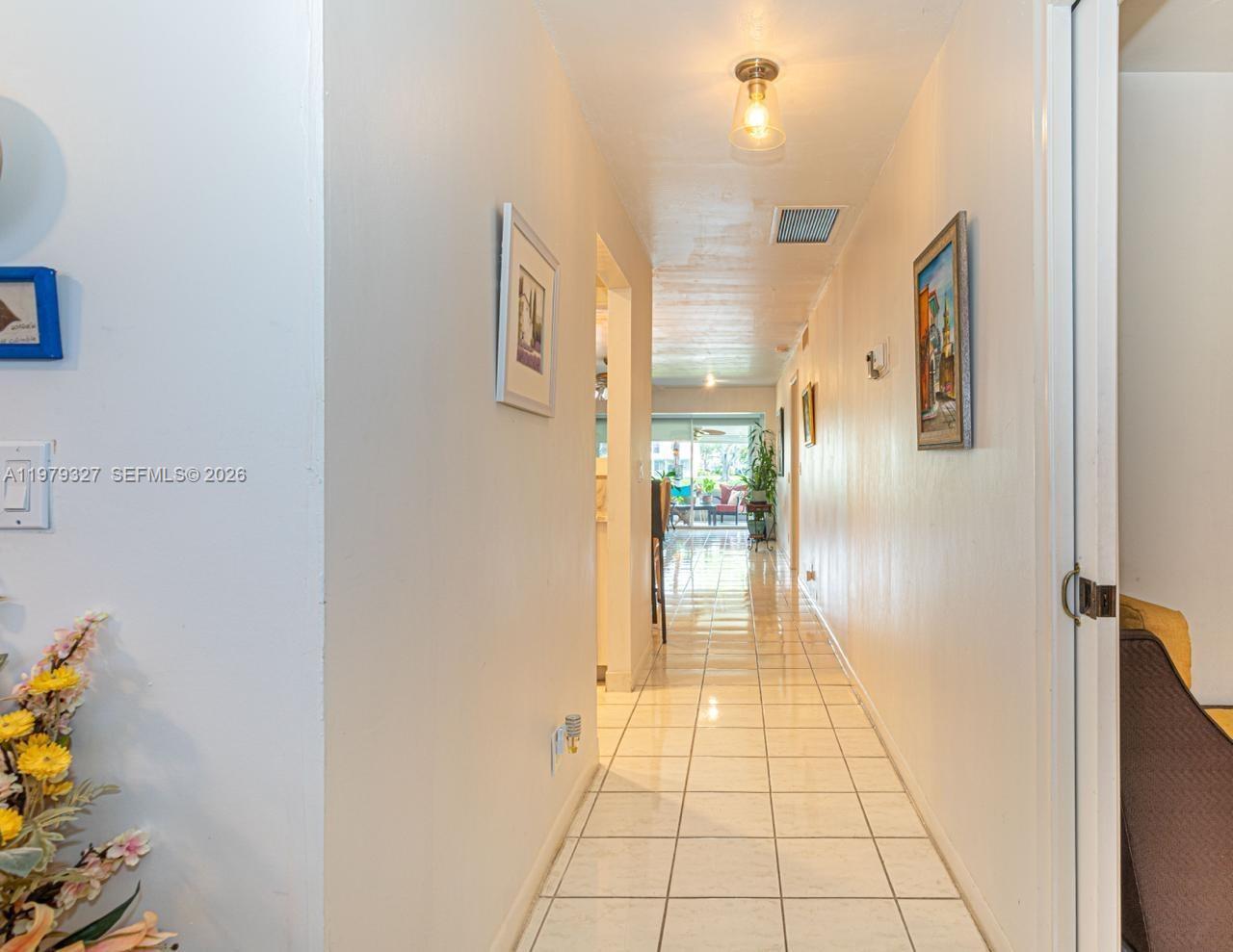 A long hallway with white walls and tiled floors leads toward a bright living area — 1421 NW 19th Ter # 102, Delray Beach FL 33445, DELRAY BEACH, FL