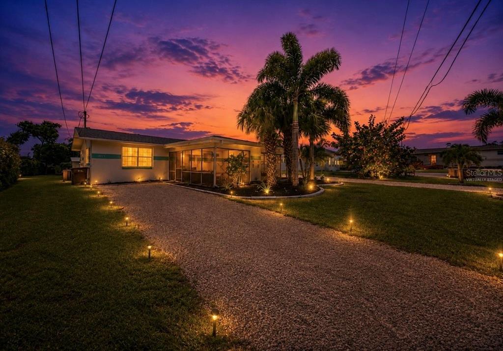A single-story house with a gravel driveway and palm trees under a vibrant sunset sky — 4931 VICTORIA DRIVE, CAPE CORAL, FL