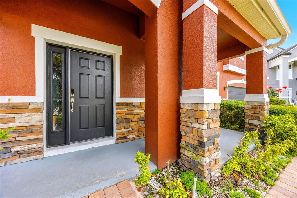 A front porch with a black door, stone accents, and orange stucco walls — 2820 CYPRESS GROVE COURT, ST CLOUD, FL