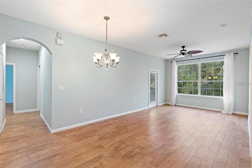 An empty room with light blue walls, hardwood floors, a chandelier, and a ceiling fan — 6265 CONTESSA DRIVE UNIT 210, ORLANDO, FL