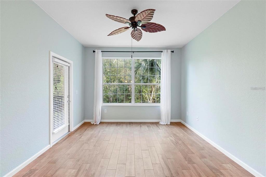 An empty room with light blue walls, wood-look flooring, a ceiling fan, and a window — 6265 CONTESSA DRIVE UNIT 210, ORLANDO, FL