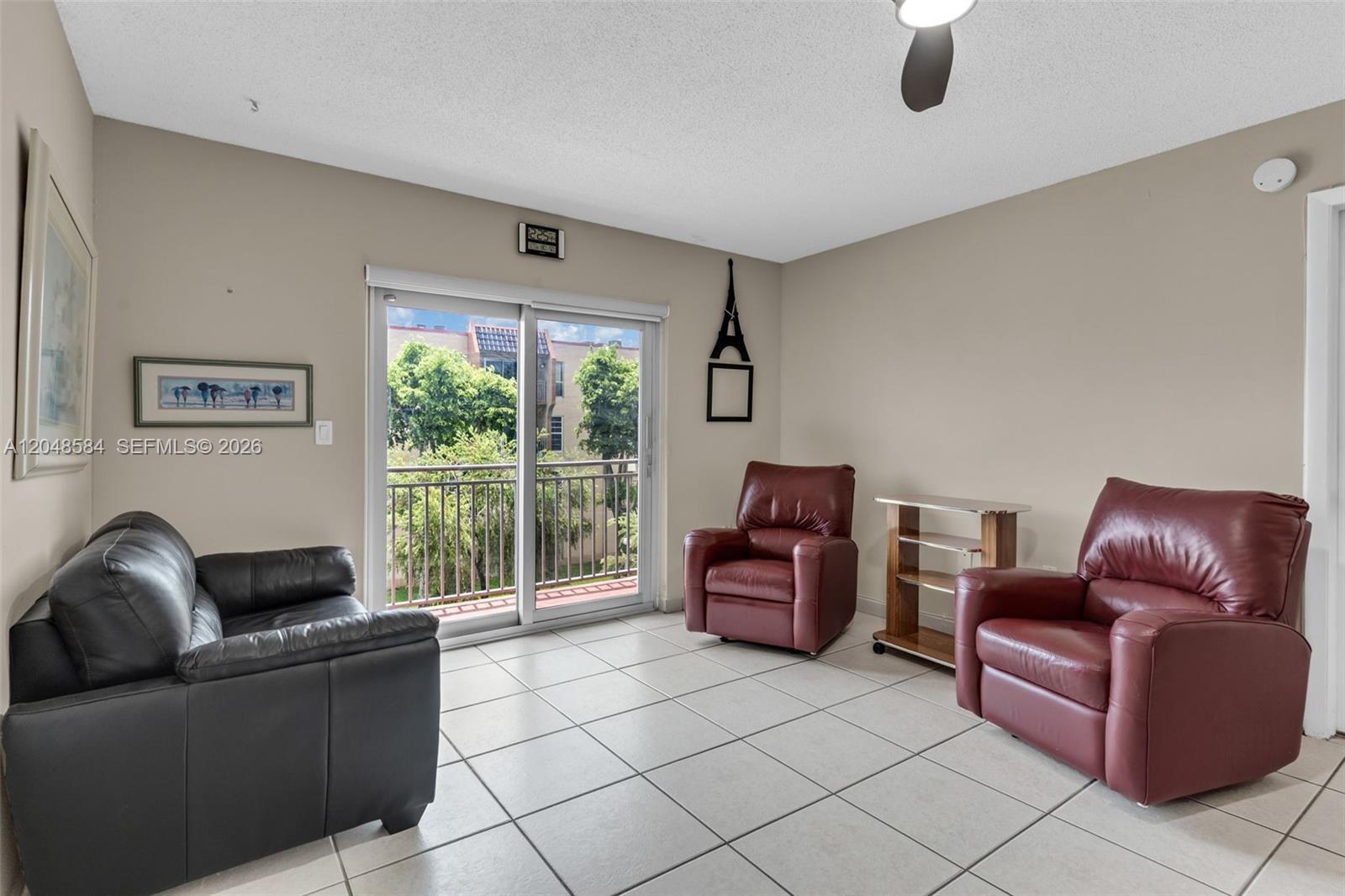 A living room features light tile flooring, beige walls, a sliding glass door, and leather seating — 4715 NW 7th St # 2, Miami FL 33126, MIAMI, FL