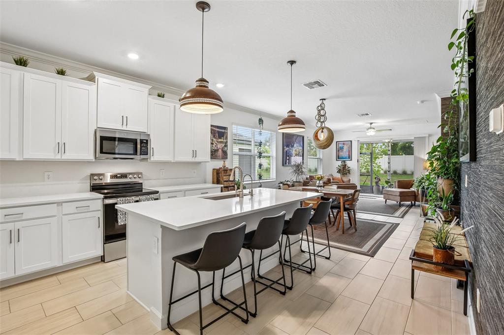 A modern kitchen with white cabinets, a central island, and an open-concept living area — 12617 LILY QUARTZ LOOP, PARRISH, FL