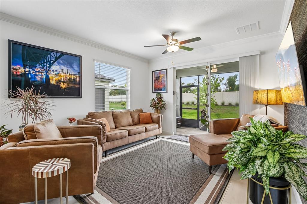 A living room features brown leather furniture, a patterned rug, and a sliding glass door — 12617 LILY QUARTZ LOOP, PARRISH, FL