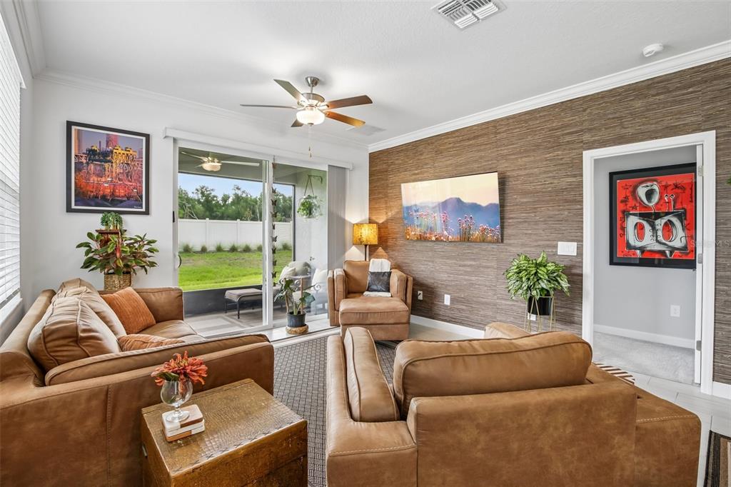 A living room features brown leather furniture, a textured accent wall, and a sliding glass door — 12617 LILY QUARTZ LOOP, PARRISH, FL