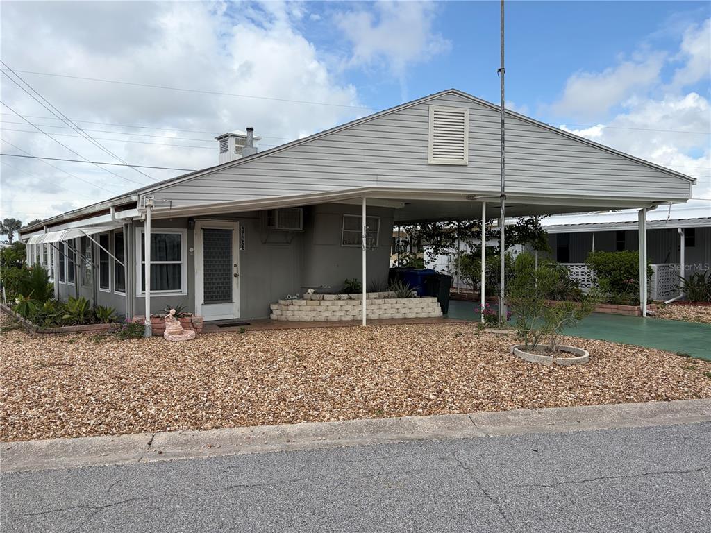 A single-story mobile home with a large attached carport and a gravel front yard — 5066 PEBBLE BEACH AVENUE, SARASOTA, FL