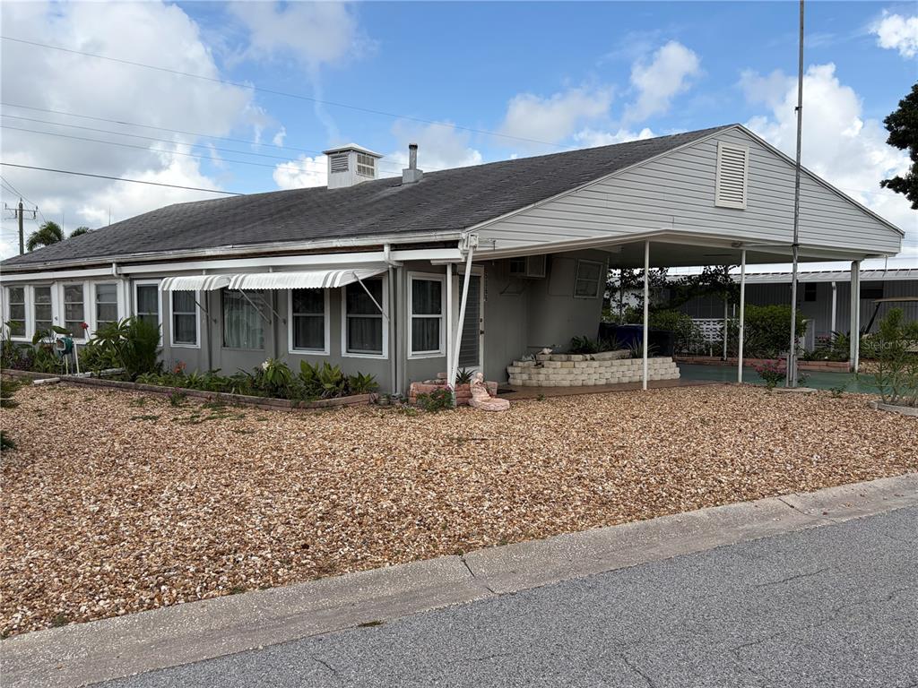 A single-story mobile home with a gravel front yard and an attached carport — 5066 PEBBLE BEACH AVENUE, SARASOTA, FL