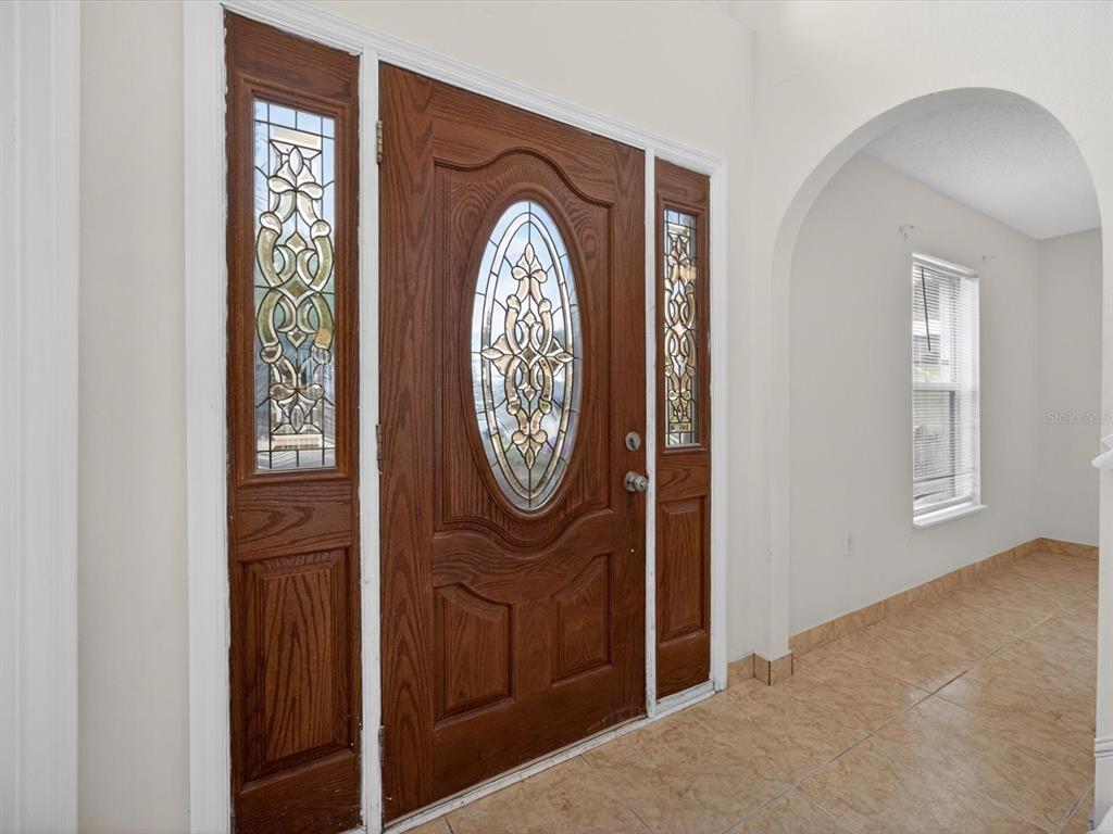 A wooden front door with decorative glass inserts is flanked by matching sidelights in a foyer — 1614 HERRING LANE, CLERMONT, FL