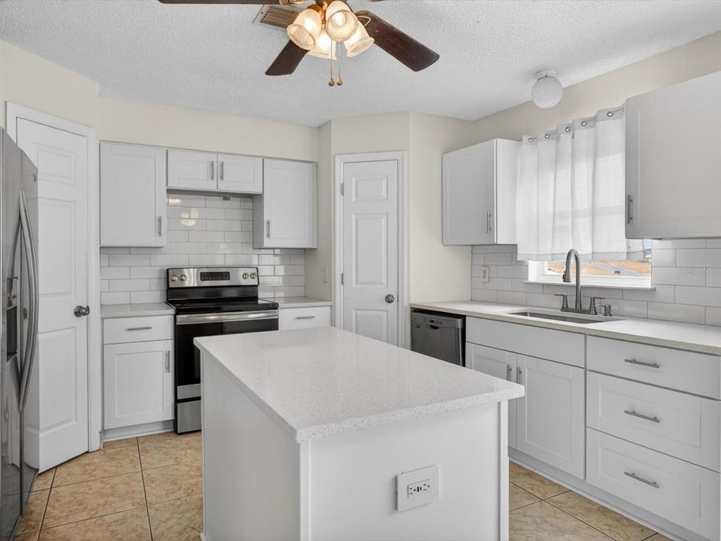 A kitchen with white cabinets, a central island, stainless steel appliances, and tile flooring — 1614 HERRING LANE, CLERMONT, FL