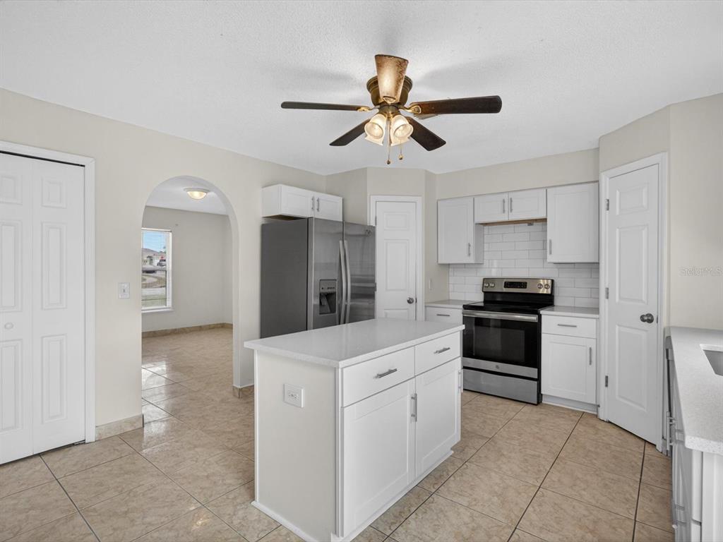 A kitchen with white cabinets, a central island, stainless steel appliances, and beige tile flooring — 1614 HERRING LANE, CLERMONT, FL