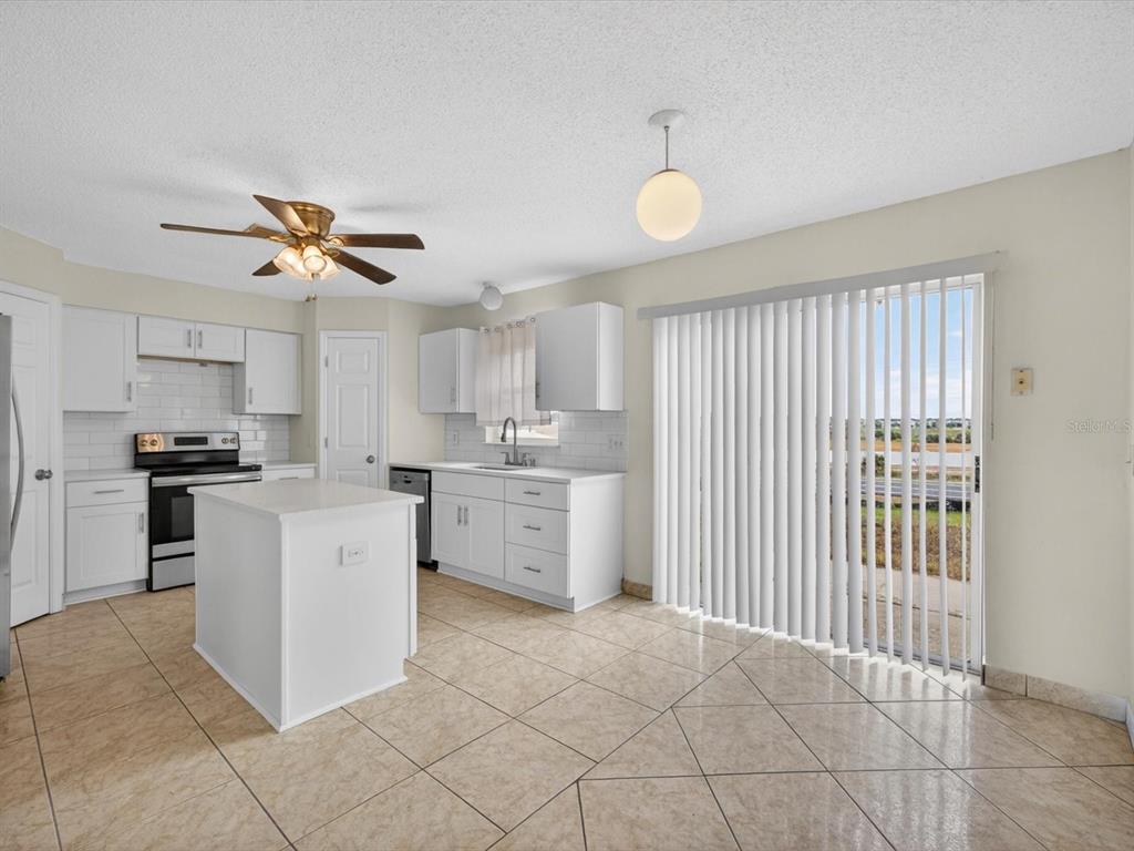 A kitchen with white cabinets, a central island, tile flooring, and sliding glass patio doors — 1614 HERRING LANE, CLERMONT, FL