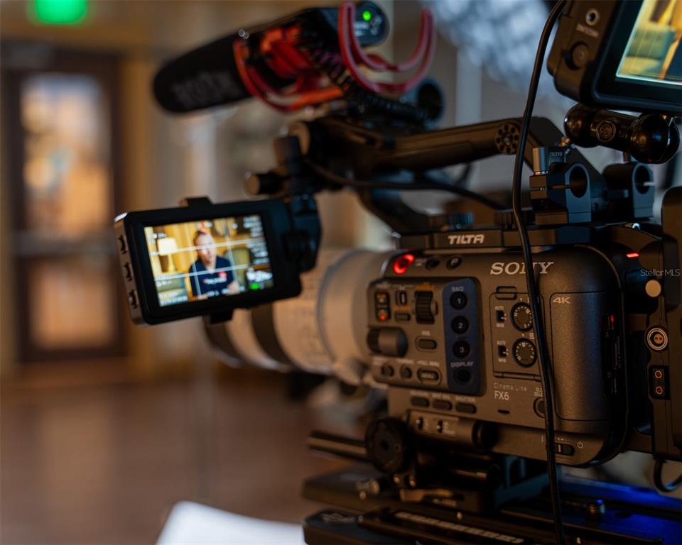 A close-up view of a professional Sony FX6 cinema camera filming a person indoors — 4705 S APOPKA VINELAND ROAD UNIT 210, ORLANDO, FL