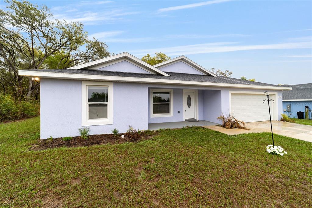 A light purple single-story house features a white front door, garage, and a grassy yard — 2349 W JUAN VEGA LANE, DUNNELLON, FL