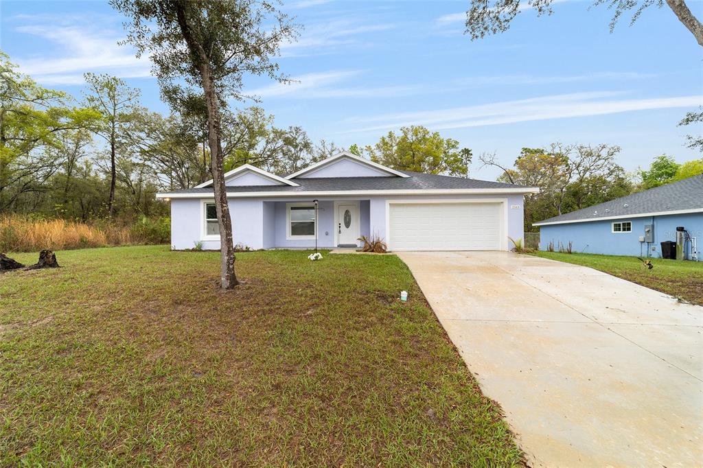 A light blue single-story house with a white garage door and a concrete driveway — 2349 W JUAN VEGA LANE, DUNNELLON, FL