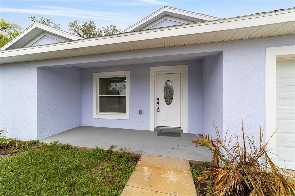A light purple house exterior features a covered porch, a white front door, and a window — 2349 W JUAN VEGA LANE, DUNNELLON, FL