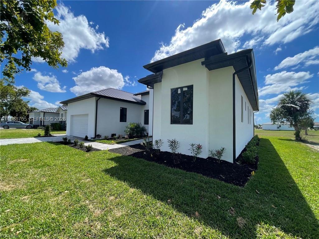 A side view of a modern white house with a dark metal roof and landscaping — 24249 Peppercorn Rd., Punta Gorda FL 33955, PUNTA GORDA, FL
