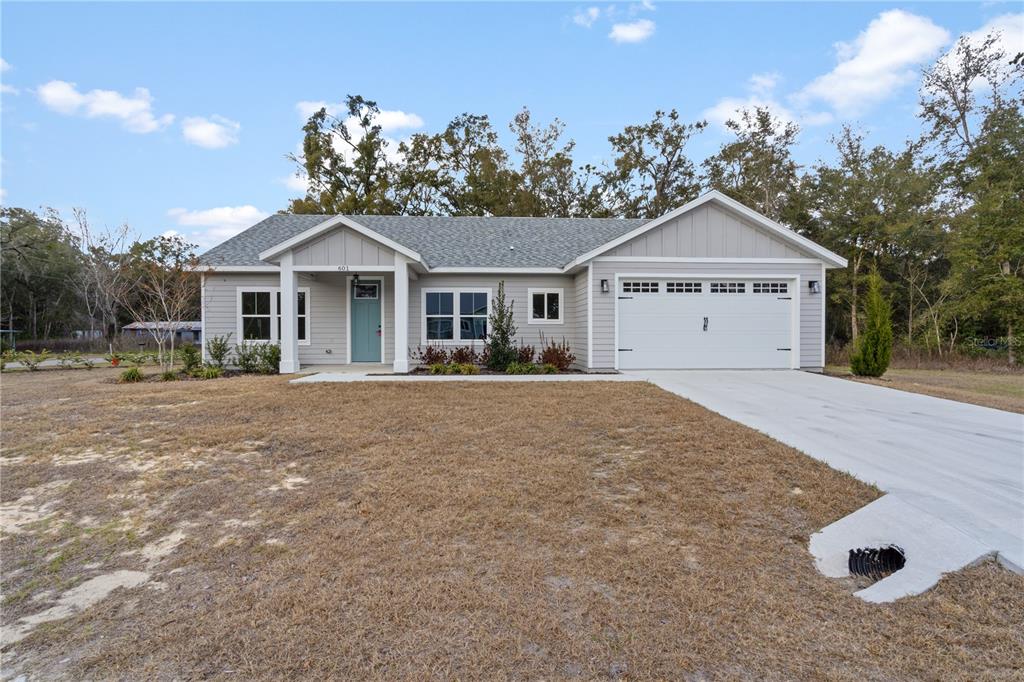 A single-story house with light gray siding, a white garage, and a teal front door — 601 FISHER DRIVE, BRONSON, FL