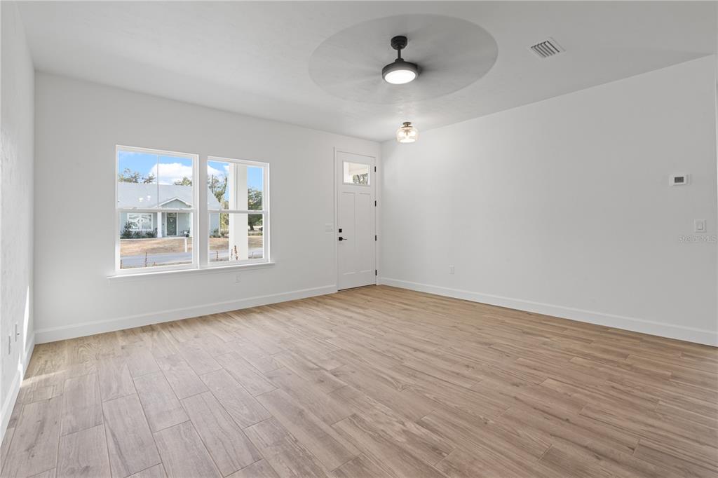 An empty room features light wood-look flooring, white walls, a ceiling fan, and a front door — 601 FISHER DRIVE, BRONSON, FL