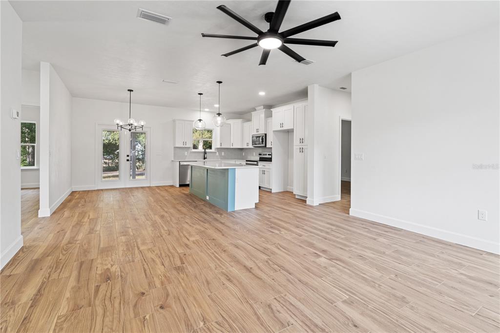 A bright, open-concept kitchen features a blue island, white cabinetry, and light wood-look flooring — 601 FISHER DRIVE, BRONSON, FL