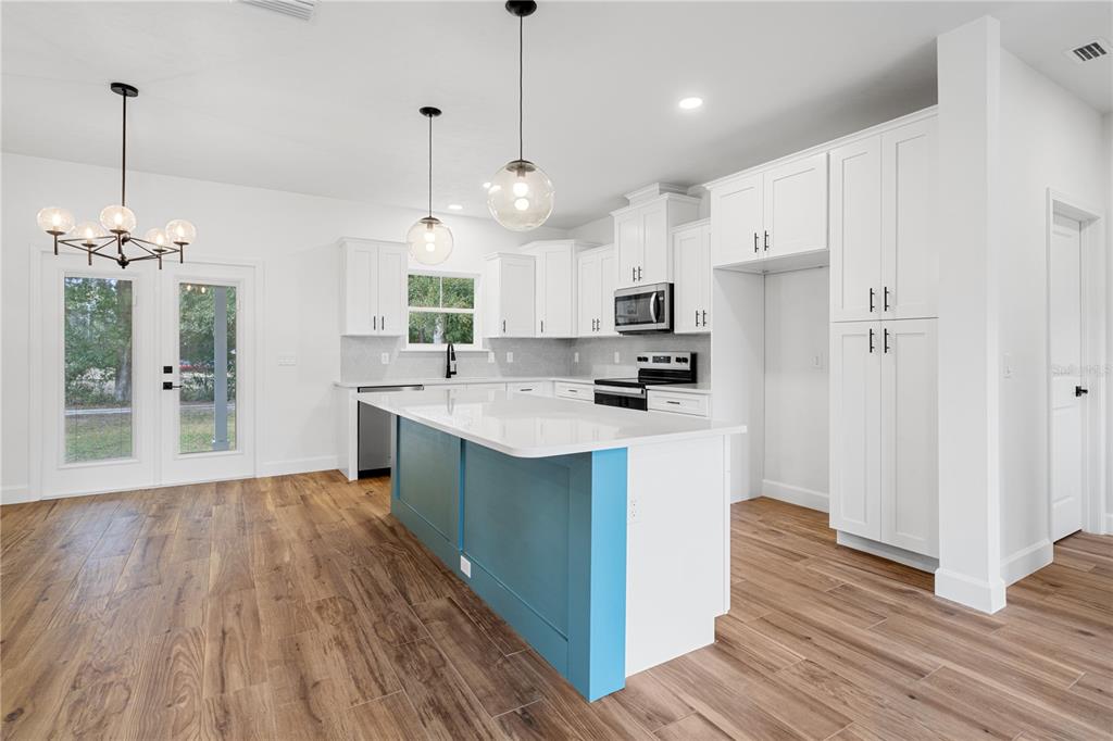 A kitchen features white cabinetry, a blue island, and wood-look flooring in an open space — 601 FISHER DRIVE, BRONSON, FL