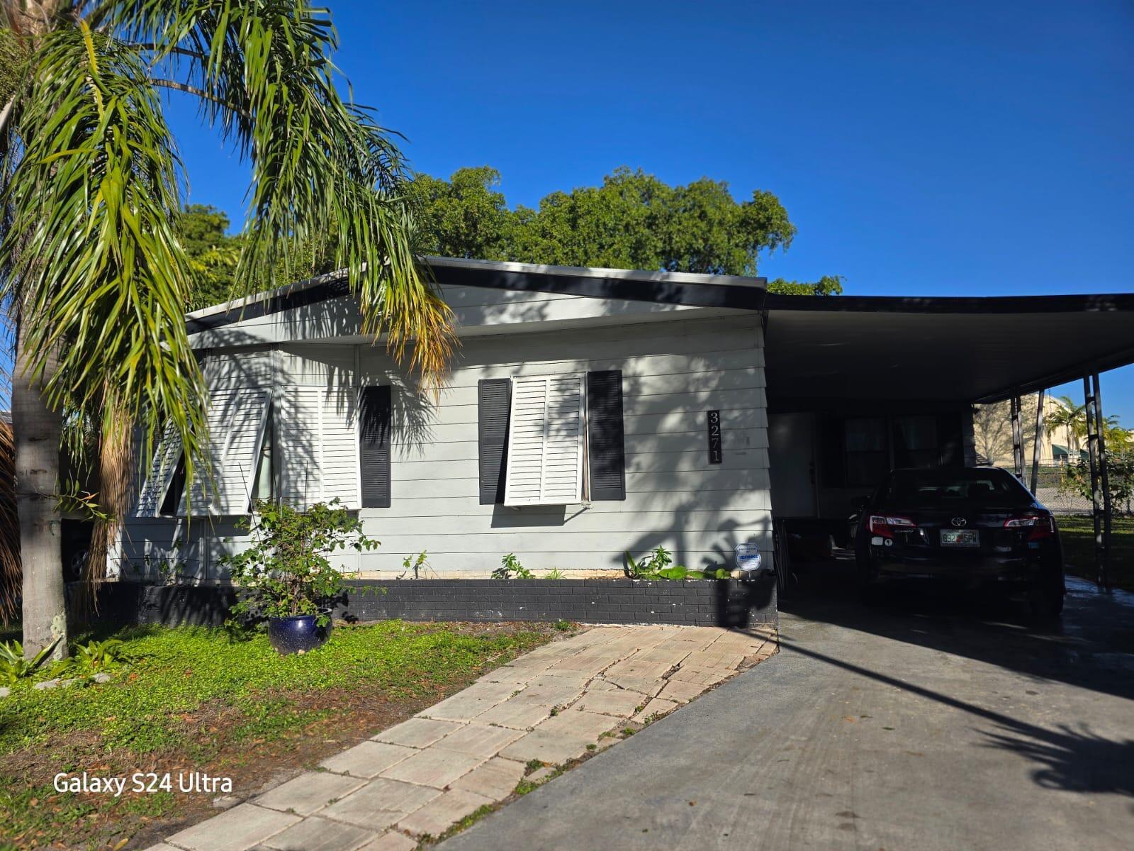 A single-story manufactured home with light gray siding, black shutters, and an attached carport — 3271 Fairway Drive, Pompano Beach FL 33069, POMPANO BEACH, FL