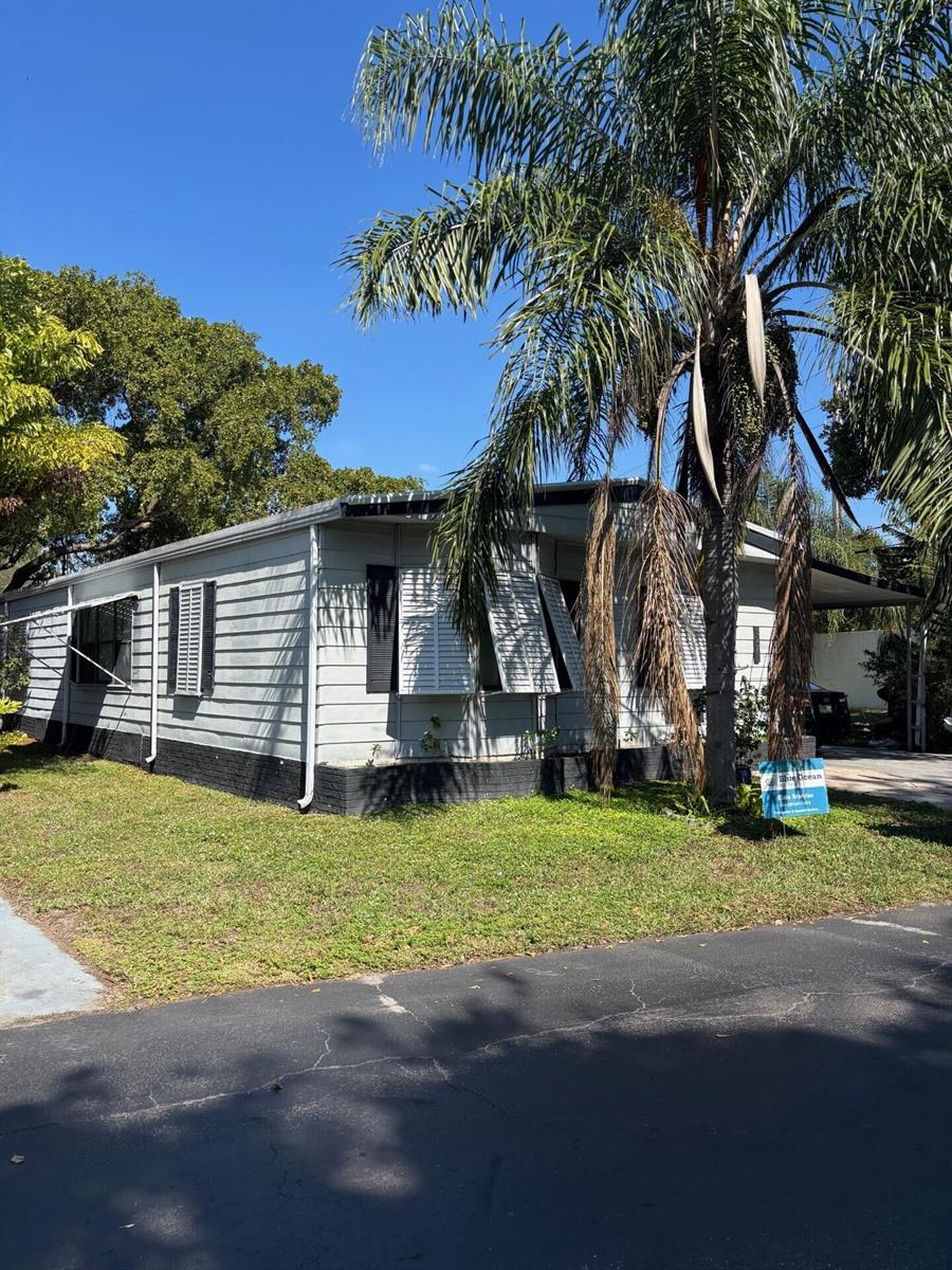 A light-colored mobile home with black trim and shutters stands beside a tall palm tree — 3271 Fairway Drive, Pompano Beach FL 33069, POMPANO BEACH, FL
