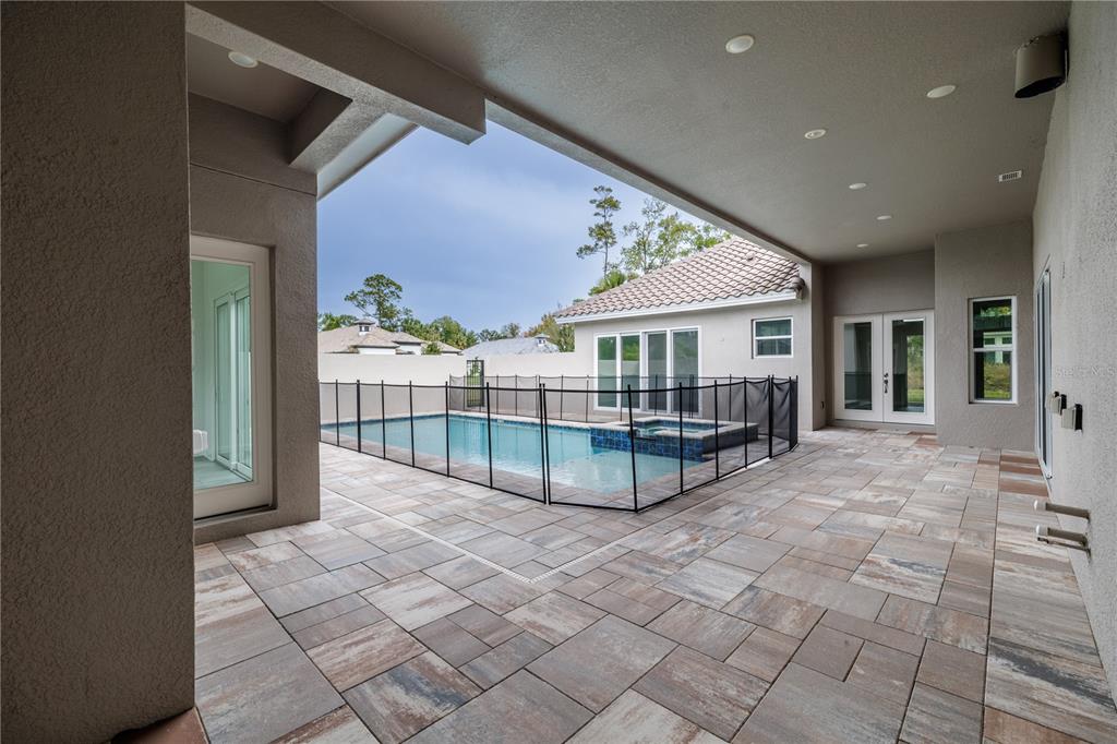 A covered patio with stone pavers overlooks a fenced swimming pool and spa — 106 NEW LEATHERWOOD DRIVE, PALM COAST, FL