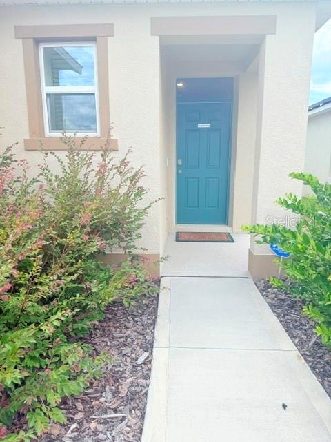 A teal front door is recessed into a beige stucco home with a concrete walkway — 2579 SAGE VALLEY WAY, WINTER HAVEN, FL