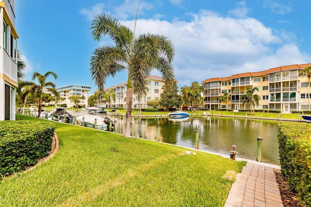 A canal view from a grassy lawn featuring palm trees, docked boats, and apartment buildings — 1250 N PORTOFINO DRIVE UNIT 302, SARASOTA, FL