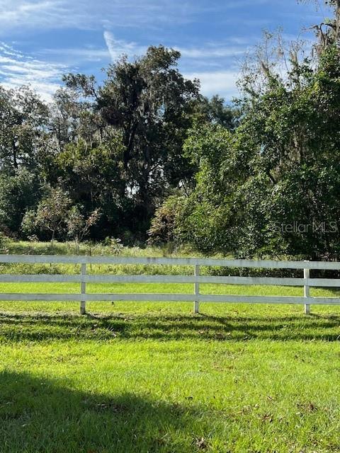 A white wooden fence separates a grassy lawn from a dense, wooded area — 16604 NW STATE ROAD 45, HIGH SPRINGS, FL