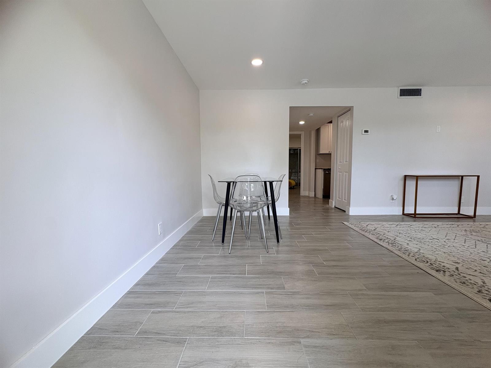A dining area with a glass table and clear chairs sits on grey tile flooring — 2202 NE 36th Street # 17, Lighthouse Point FL 33064, LIGHTHOUSE POINT, FL
