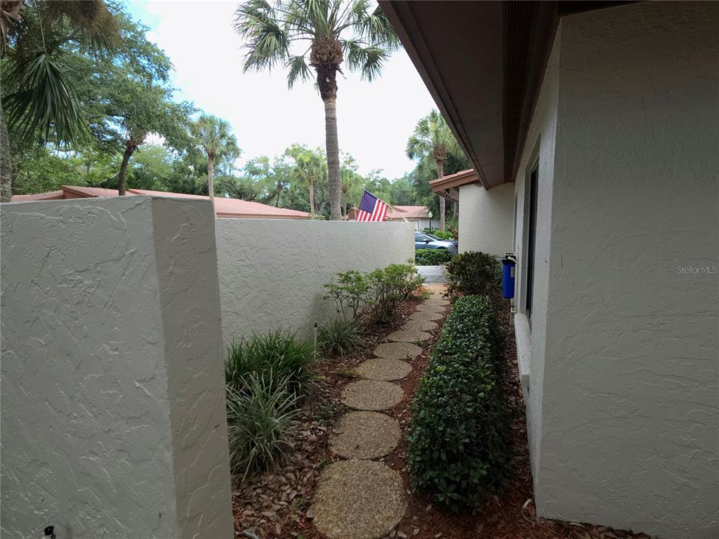 A stone path leads between a stucco wall and a house exterior with landscaping — 6402 MEADOWLARK LN, BRADENTON, FL