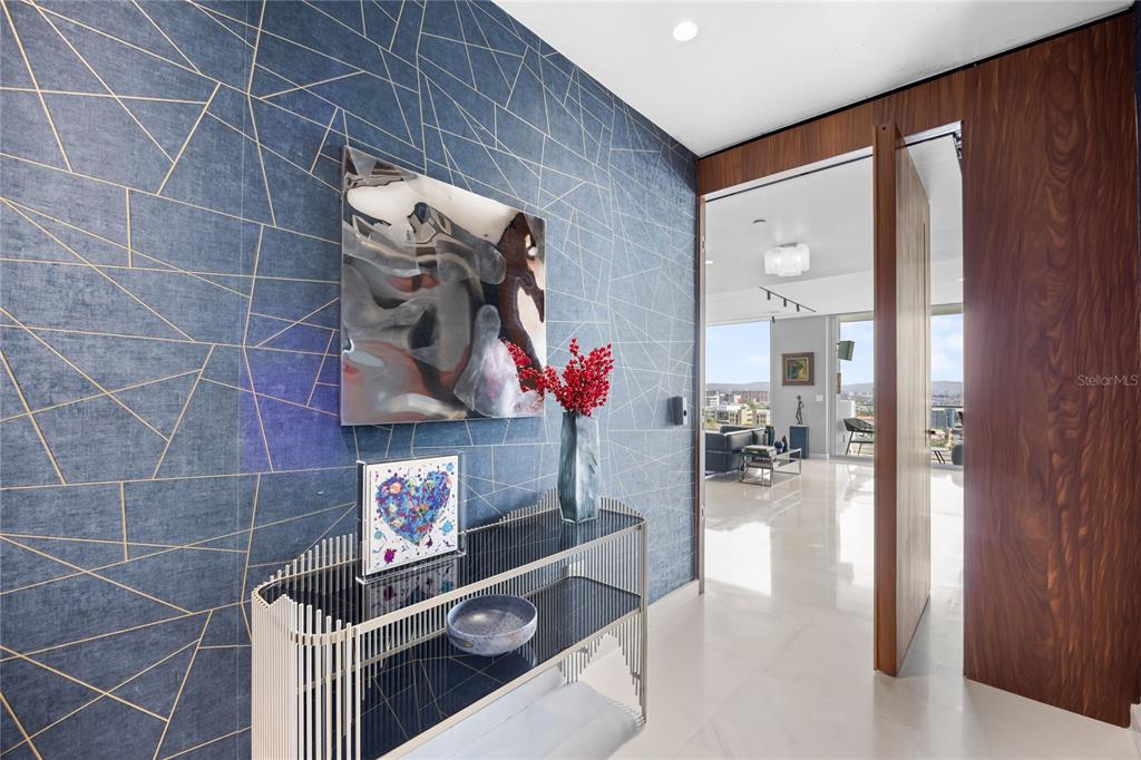 A modern entryway features blue geometric wallpaper, a metal console table, and a wood-paneled doorway — 1002 ASHFORD AVENUE UNIT 14, CONDADO, PR
