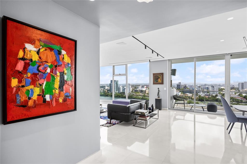 A modern living room features a large abstract painting, white tile floors, and floor-to-ceiling windows — 1002 ASHFORD AVENUE UNIT 14, CONDADO, PR