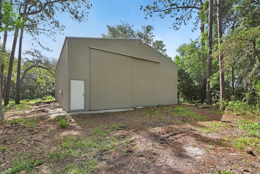 A metal workshop building with a sliding door and a white entry door in woods — 1530 DEERMOSS LANE, DELAND, FL