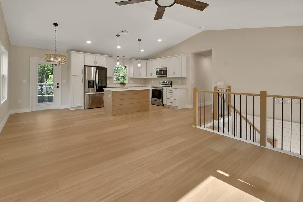 An open-concept kitchen features white cabinetry, a wood-paneled island, and light wood flooring — 1530 DEERMOSS LANE, DELAND, FL