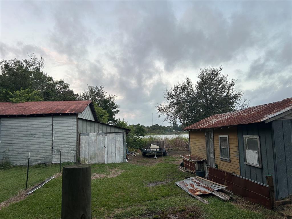 Two weathered sheds with rusted metal roofs stand on a grassy lot near water — 2844 LAKE ALFRED ROAD, WINTER HAVEN, FL