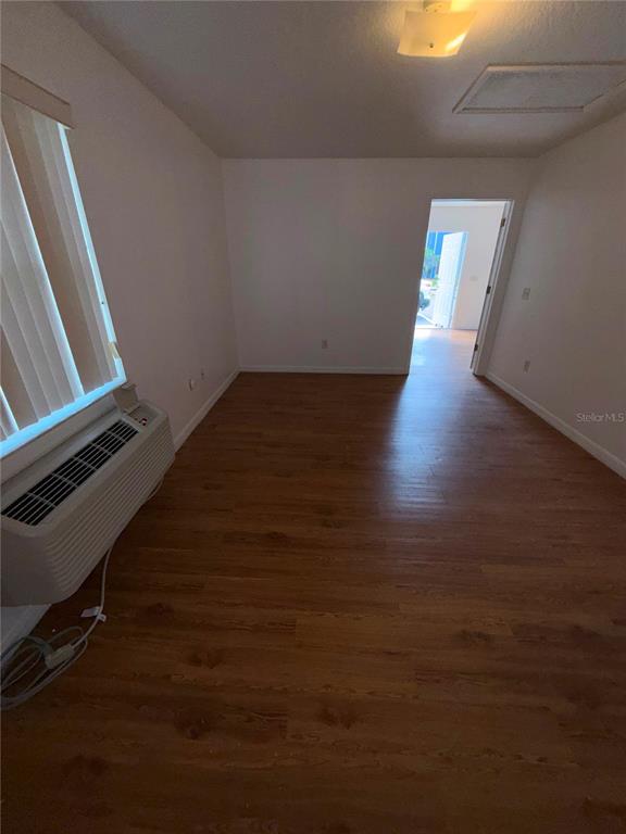 An empty room with wood-look flooring, a wall-mounted air conditioner, and a doorway leading outside — 862 CARIBBEAN DRIVE UNIT B, DAVENPORT, FL