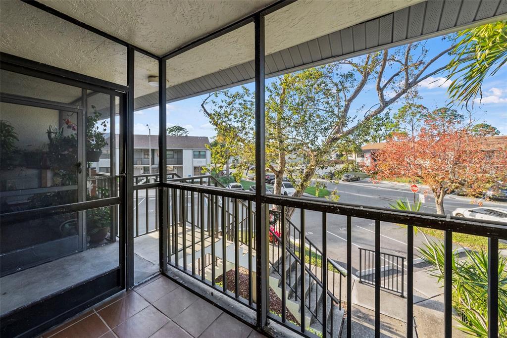 A screened-in balcony with tiled flooring overlooks a parking lot and outdoor staircase — 1918 PELICAN LANDING BOULEVARD UNIT 1125, CLEARWATER, FL