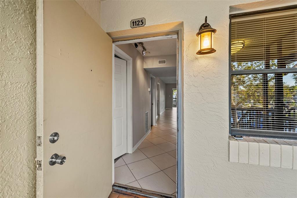 An open front door reveals a tiled entryway and hallway leading into a residential unit — 1918 PELICAN LANDING BOULEVARD UNIT 1125, CLEARWATER, FL